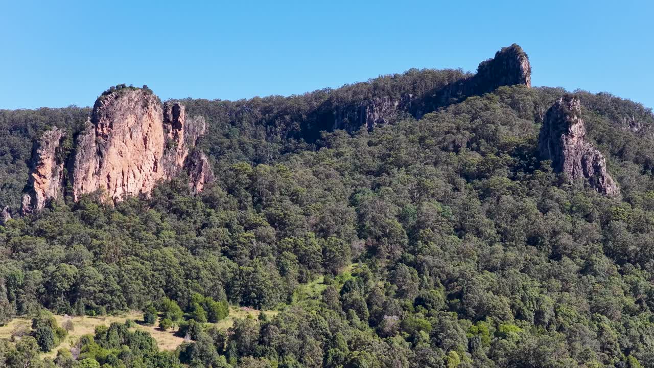 Drone footage captures lush green hills and rocky formations under clear blue skies in Nimbin, Australia