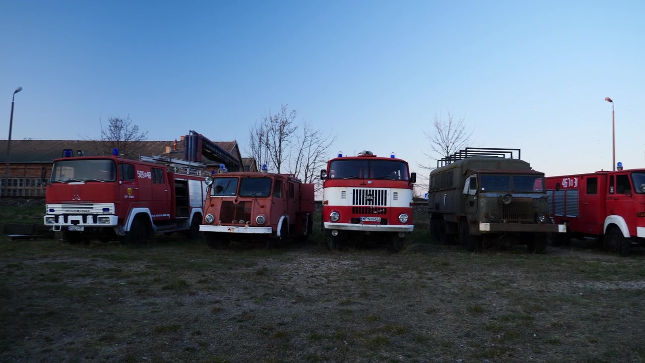 Fileira de antigos caminhões de bombeiros e veículos militares em um terreno baldio de Władysławowo ao anoitecer. Polônia.