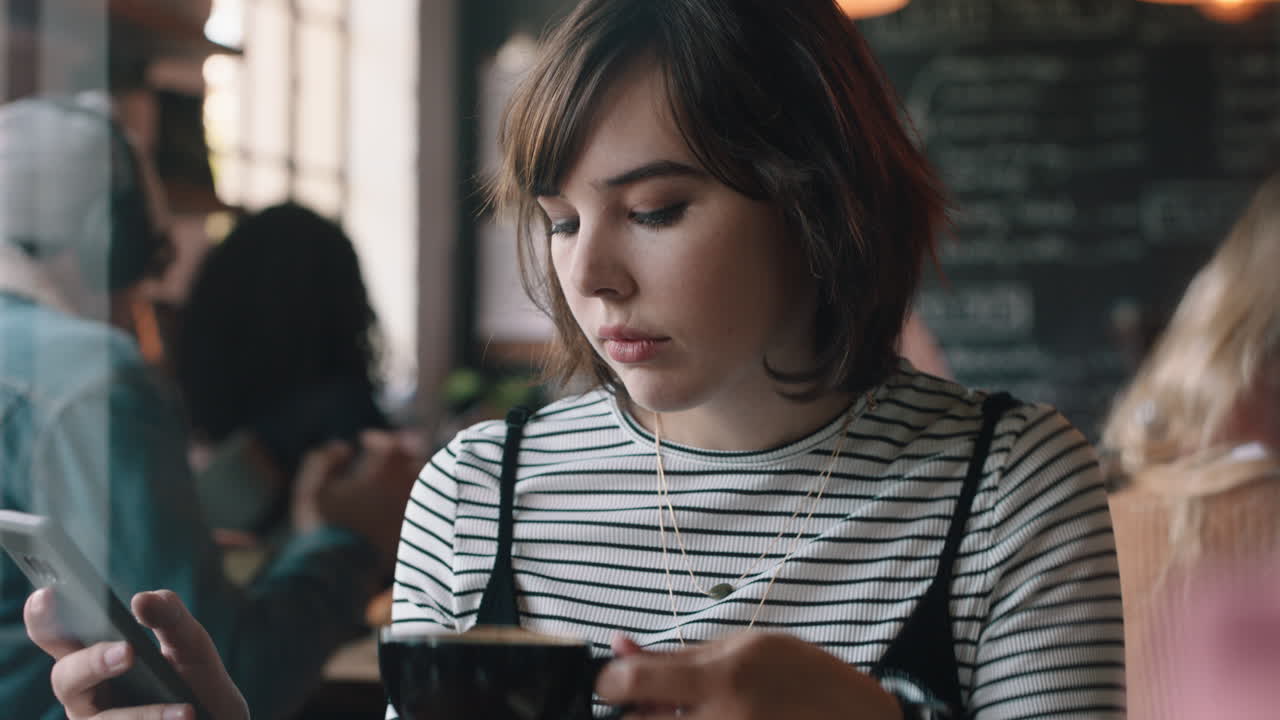 스마트폰을 사용하는 젊은 여성이 카페에서 커피를 마시고 소셜 미디어에서 메시지를 공유하고 모바일 기술을 즐기고 있습니다.