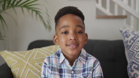 Afroamerikanischer-Junge-Sitzt-Auf-Dem-Sofa,-Blickt-In-Die-Kamera-Und-Lächelt