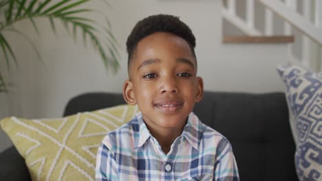 african american boy siting on sofa, looking at camera and smiling