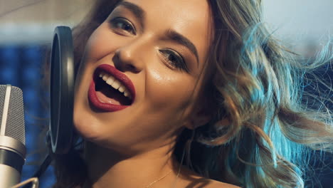 attractive face of a professional singer near microphone looking at camera and singing at music studio. portrait of a beautiful female and mic. close-up