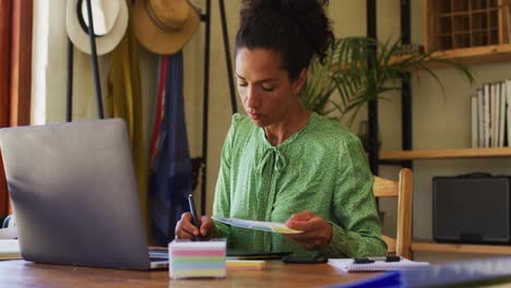 Mixed-race-woman-taking-notes-while-working-from-home