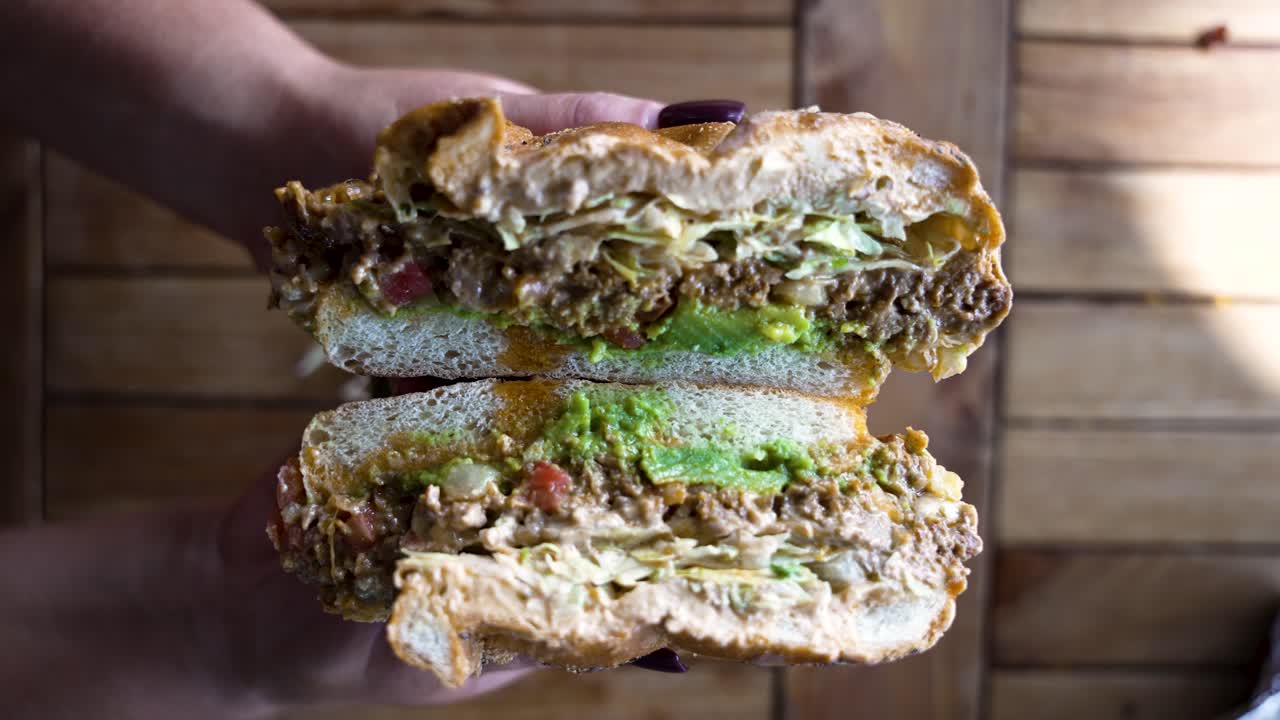 A close up of a NYC bodega style Chopped Cheese Sandwich being pulled apart in slow motion by hands with a perfect manicure to reveal the fillings