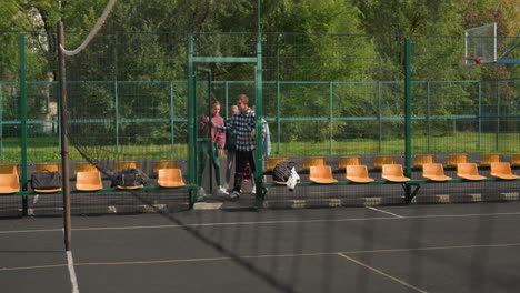 entrenador y jóvenes jugadores de voleibol abriendo la puerta a la cancha al aire libre, participando en la rutina de calentamiento con expresiones emocionadas, en un telón de fondo verde exuberante