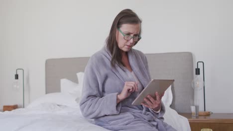 mujer con gafas usando tableta digital en la cama en casa