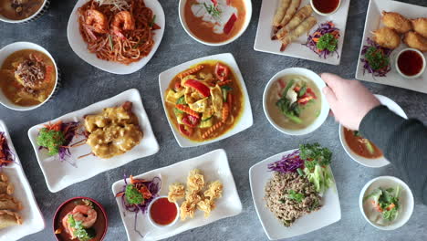 male hand rotating small bowl of thai cuisine on flat lay table top