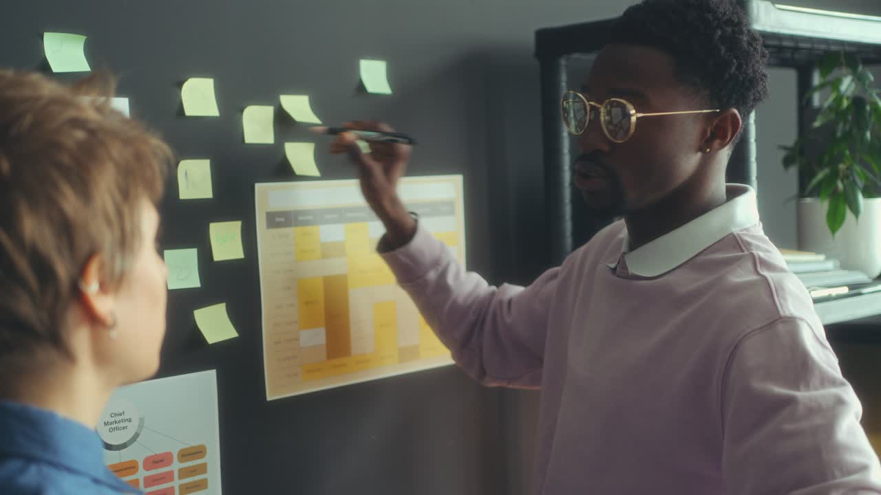 Two Diverse Colleagues Discussing Business Plans on Sticky Notes