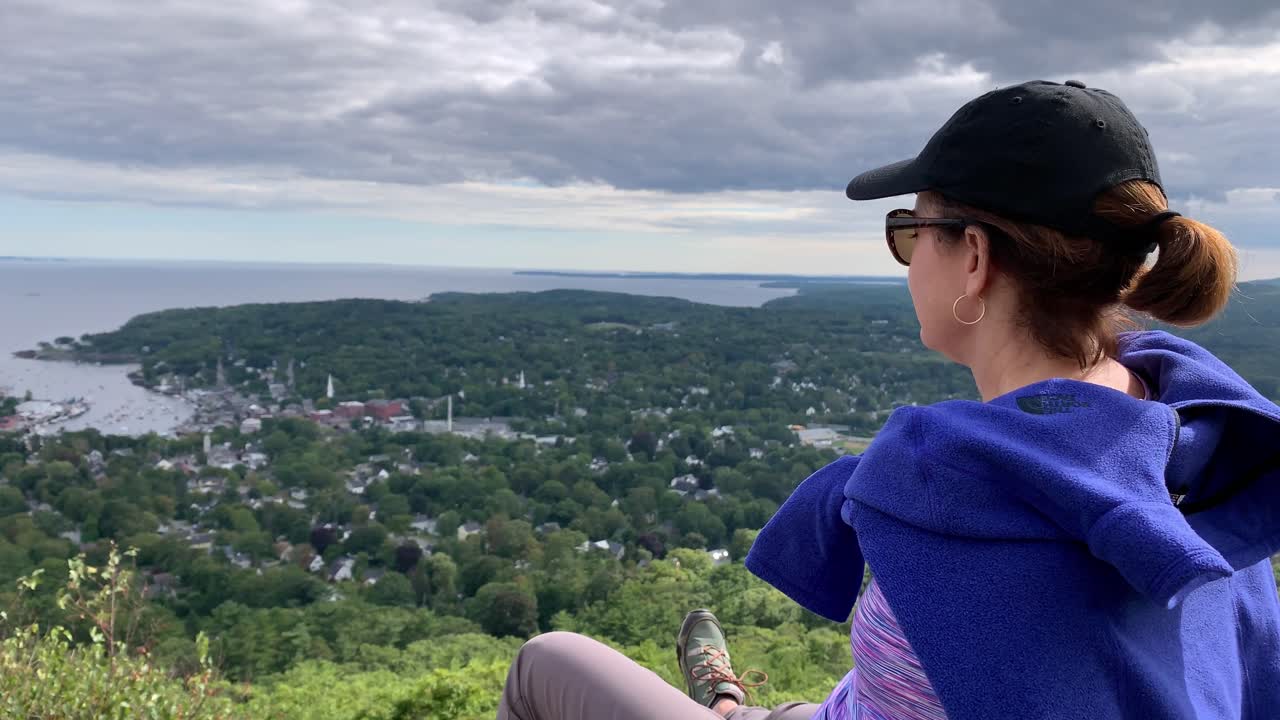 4k shot of woman looking down on Camden Maine from Mount Battie