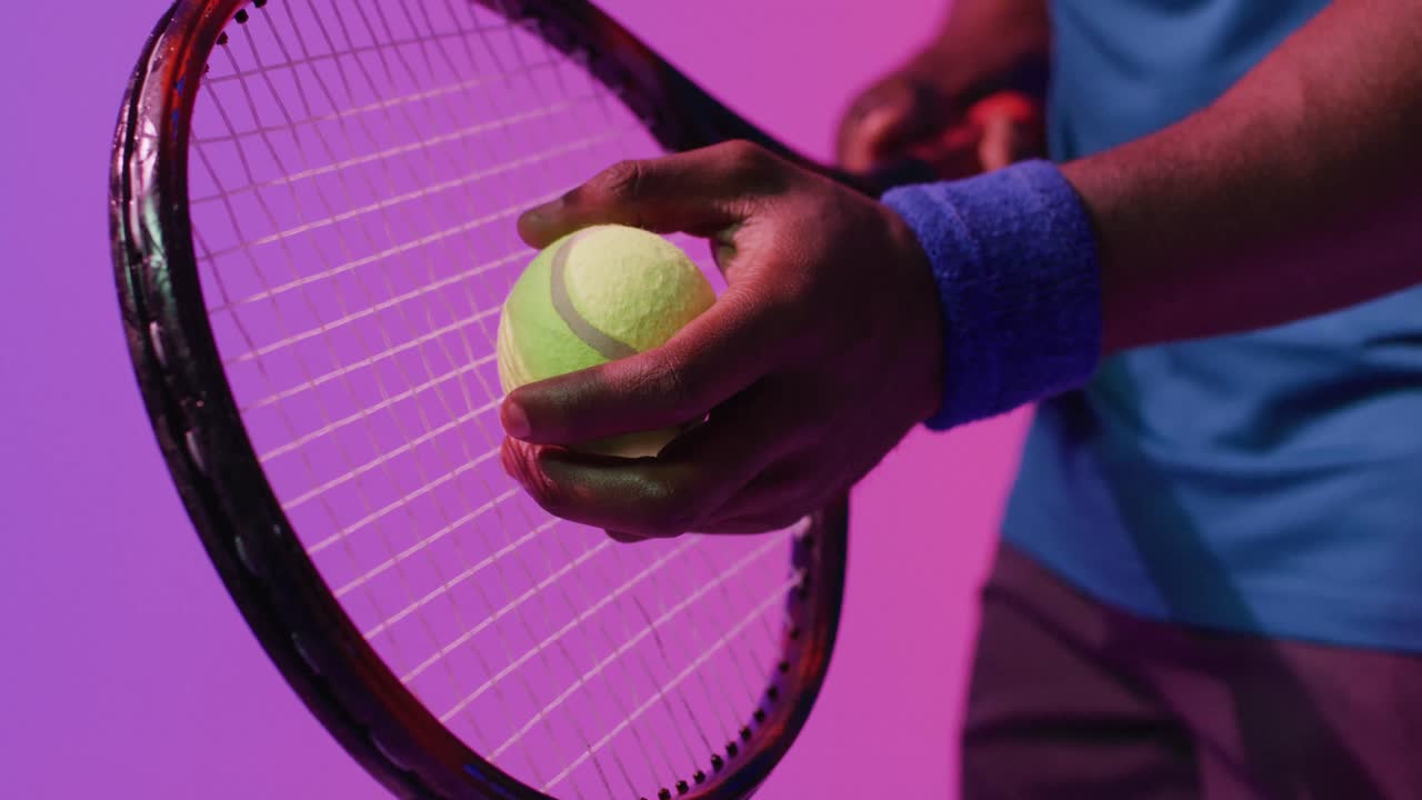 Video of hands of african american male tennis player holding racket in neon pink lightning