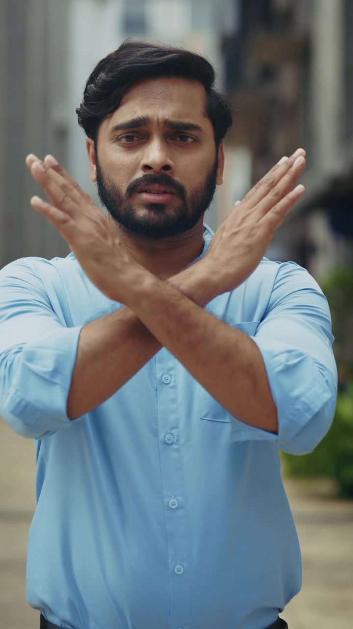 A serious Indian man crosses his arms in an outdoor portrait