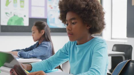 Video-of-concentrating-african-american-schoolboy-sitting-at-desk-using-tablet-in-class,-copy-space