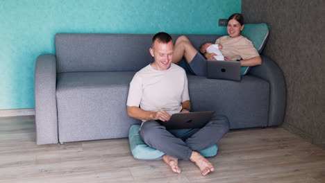 husband and wife having a newborn baby work at laptops. couple combining job with childcare.