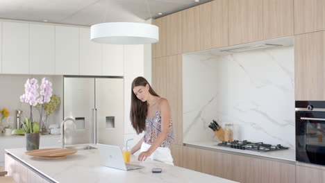 Teenage-Caucasian-girl-with-long-brown-hair-is-using-a-laptop-in-a-modern-kitchen