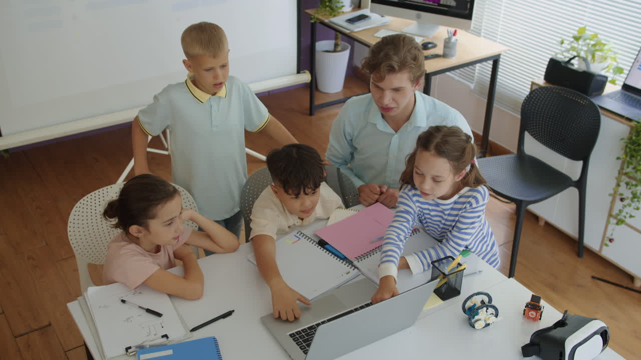 Male Teacher and Small Group of Students Doing Test on Laptop at Class