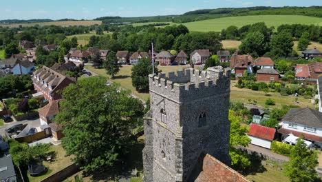 A-relaxed-arc-shot-of-Chartham,-focused-on-the-tower-of-St-Mary's-church,-flying-the-union-flag