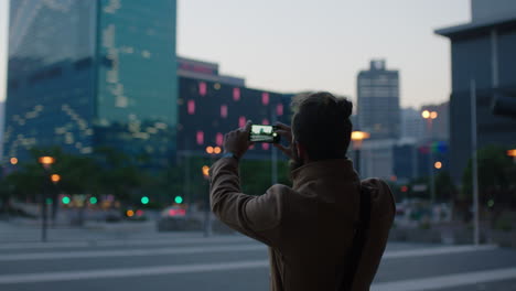 Un-Apuesto-Joven-Hipster-Tomando-Fotos-Del-Horizonte-De-La-Ciudad-Usando-Tecnología-Móvil-De-Teléfono-Inteligente-Disfrutando-Del-Estilo-De-Vida-Urbano