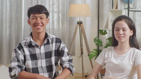 close up of asian boy and girl smiling and showing arms crossed gesture to camera while discussing with friends at home