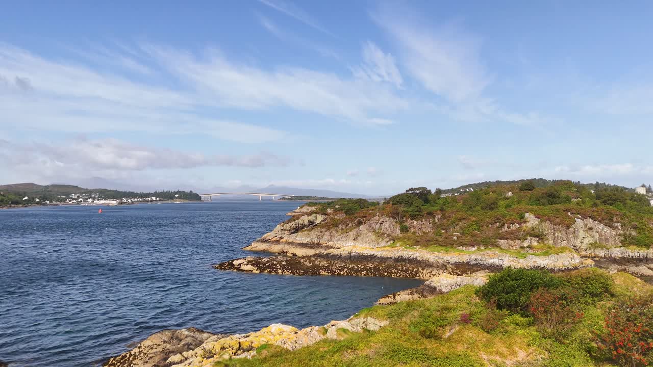 Camera pans over rugged coastline, blue sea, and lighthouse beneath clear Isle of Skye skies
