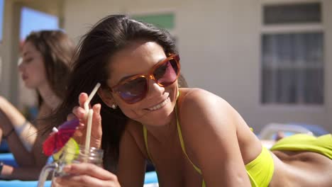 beautiful young girl in sunglasses drinking cocktails with her female friends relaxing by the pool. summertime pool party. slowmotion shot