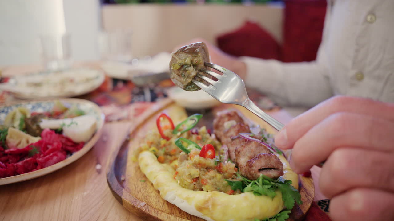 Nahaufnahme einer Frau, die gegrilltes Fleisch auf Fladenbrot schneidet, serviert mit cremiger Soße und Gemüse.