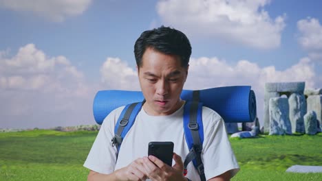 close up of asian male hiker with mountaineering backpack looking at the smartphone and saying wow while traveling in stonehenge