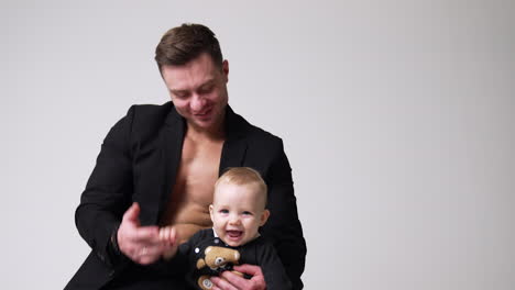 happy caucasian man in black jacket holding a cute smiling baby. father and son smiling. studio footage. white backdrop.