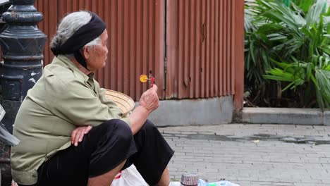 elderly person seated, vending on sidewalk