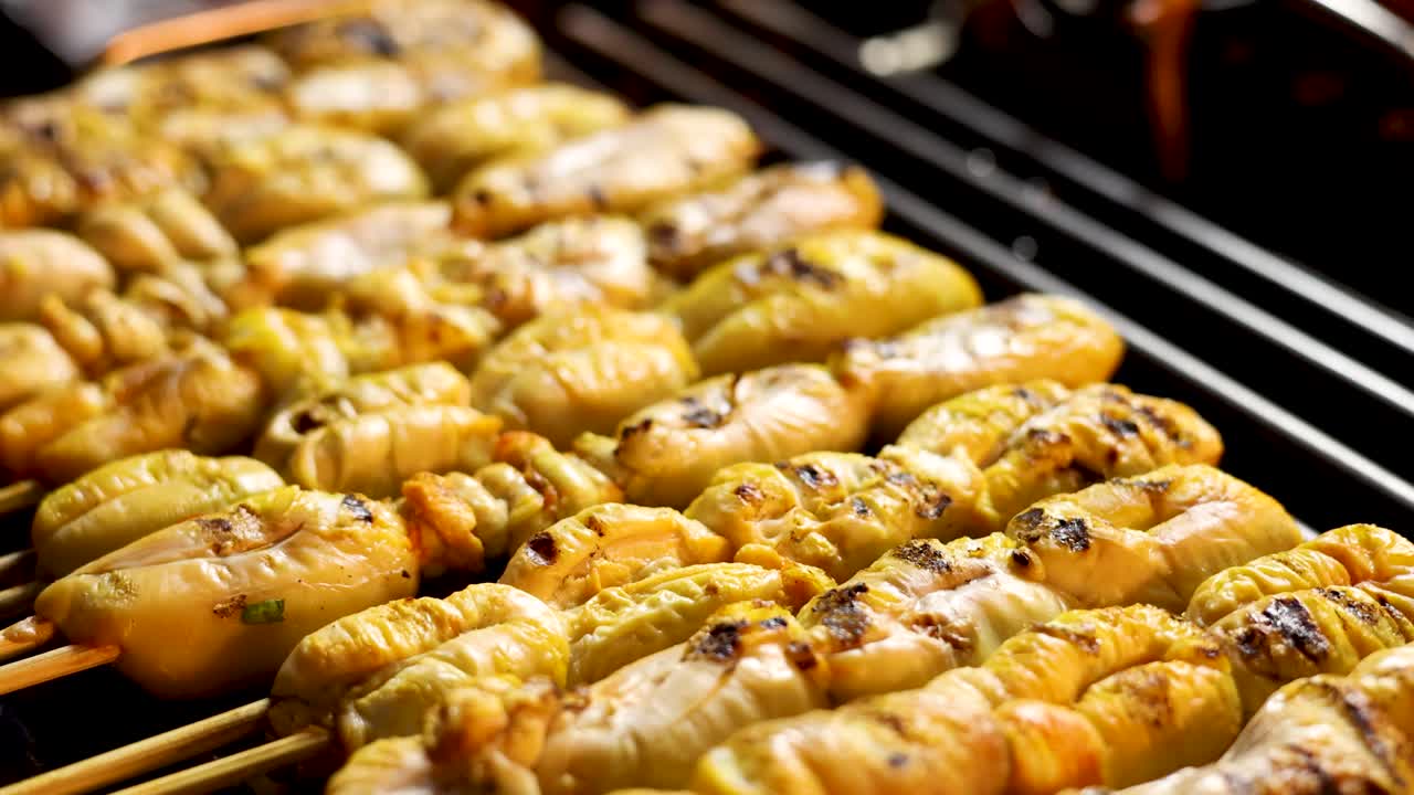 Rows of squid roe skewers grilling over open flame, close-up, warm lighting, shallow depth