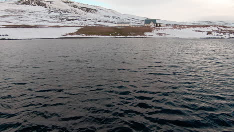 Dolly-forward-above-man-paddling-to-shore-on-kayak,-towards-house-on-hill