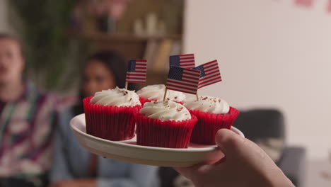 Frau-Zu-Hause-Serviert-Cupcakes-Mit-Miniatur-Amerikanischen-Stars-And-Stripes-Flaggen-An-Freunde-Auf-Party-Feiern-4.-Juli-Unabhängigkeitstag-2