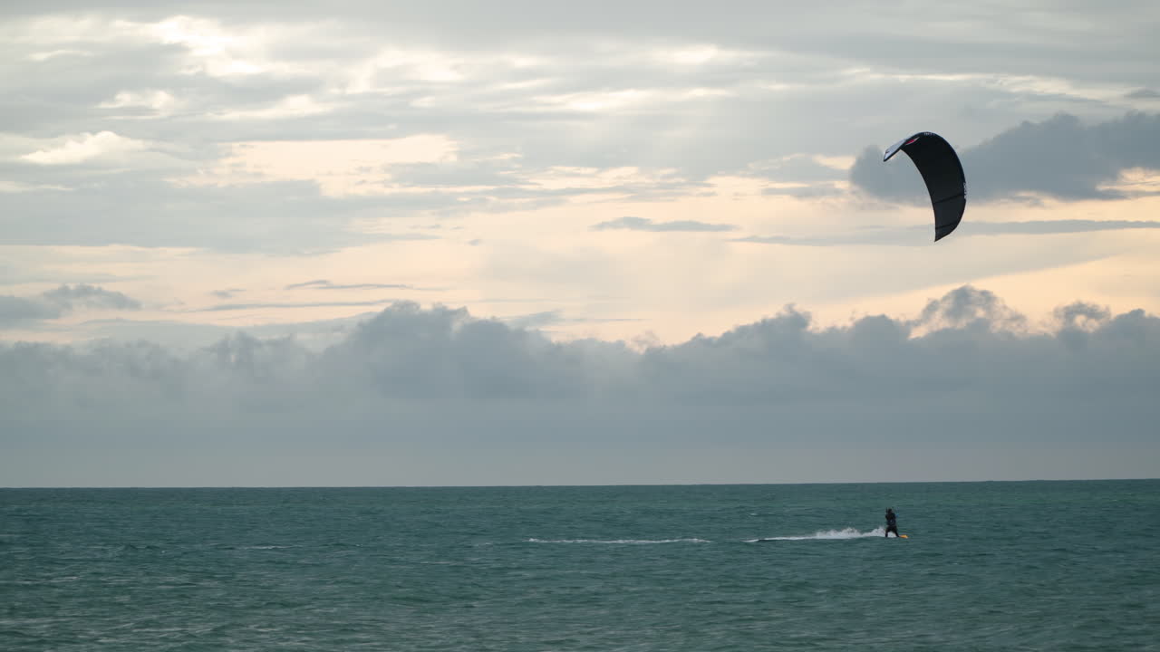 hombre haciendo kitesurf en mar abierto por la noche con un espectacular cielo nublado al atardecer - vista de seguimiento de gran angular