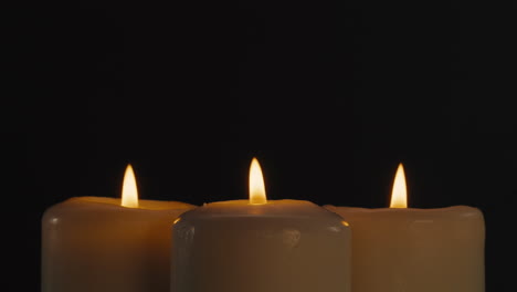 three burning candles on black background