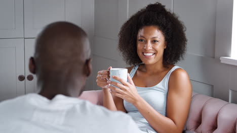Young-mixed-race-couple-relax-together,-drinking-coffee-and-talking-in-their-living-room,-boyfriend’s-back-to-camera,-close-up,-selective-focus