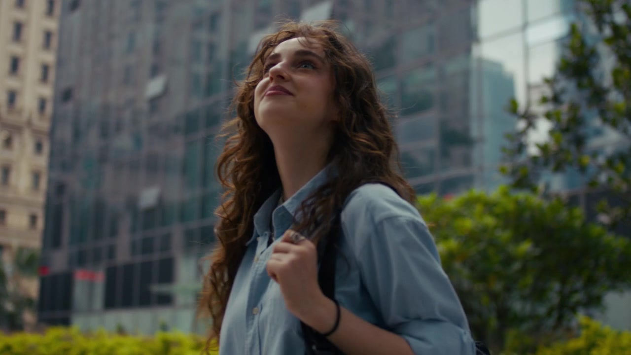 Young woman walks through modern city street, looking up at tall glass buildings