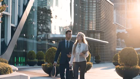two confident business people walking out of office building, talking and spending time together outside. business partners discussing work issues on the go - slow motion