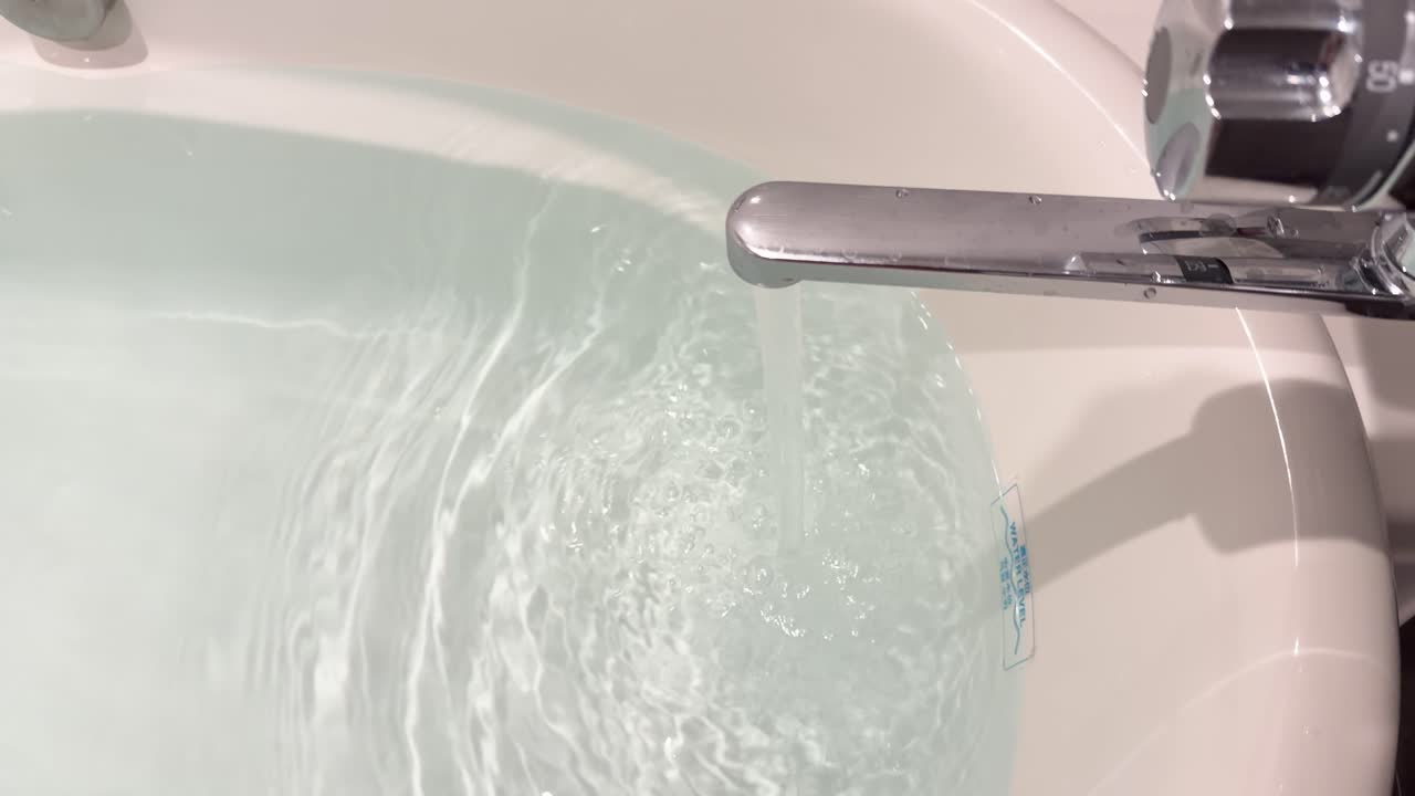 Una ripresa ravvicinata dell'acqua che scorre da un rubinetto cromato in una vasca da bagno bianca.
