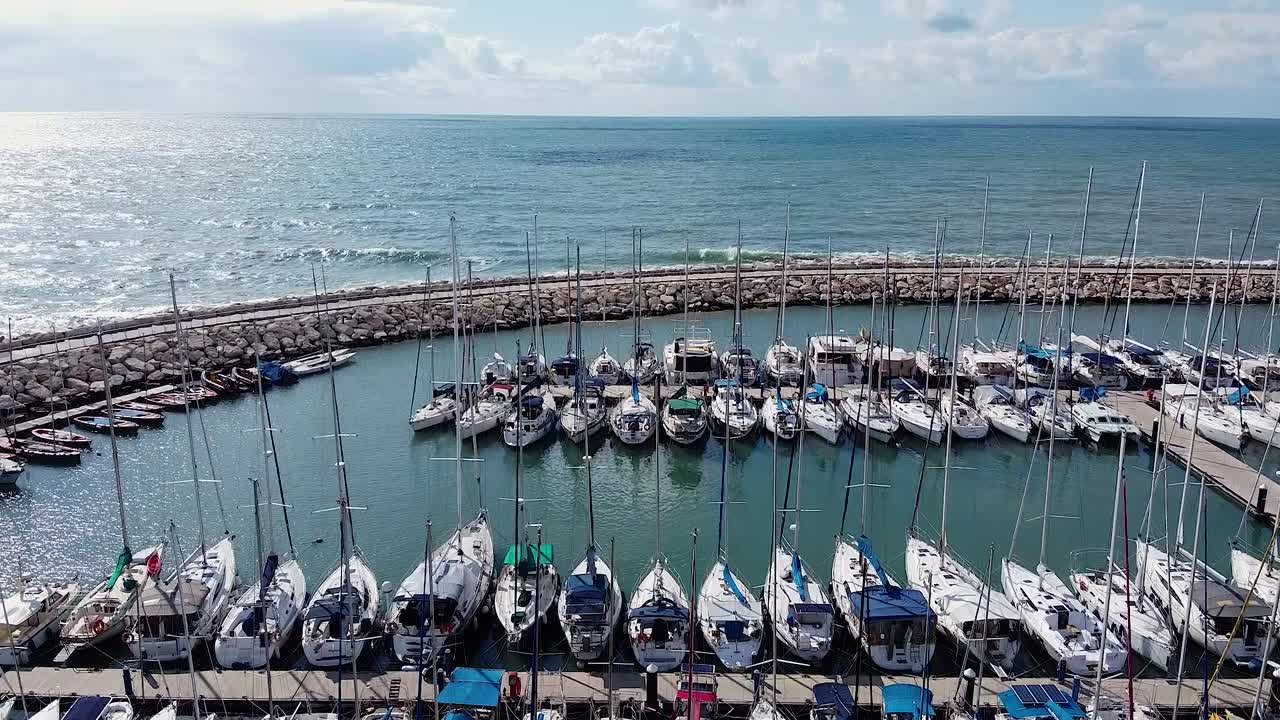 Aerial view of Tel Aviv port with anchored sailboats on a sunny day, stunning coastal scenery, flyover