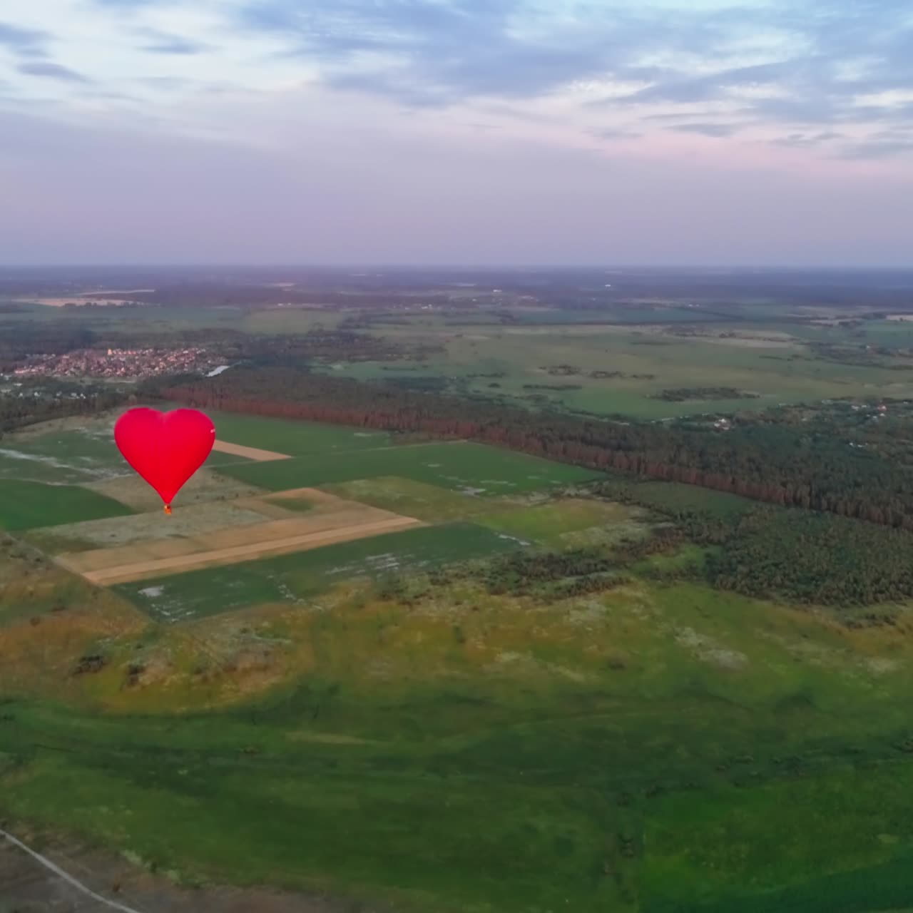 Red air balloon in love heart shape. Panoramic view on nature landscape and beautiful hot air balloon. Bright aerostat flying over the fields.