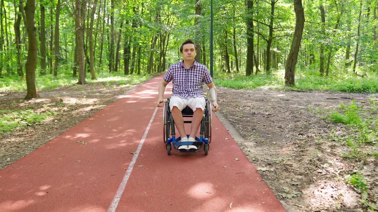 Giovane uomo in sedia a rotelle che si muove lungo un sentiero in un parco verde