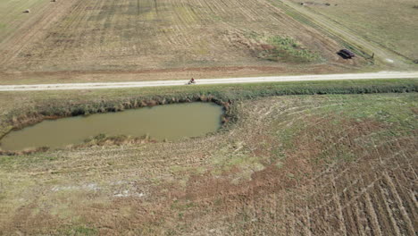 Toma-Aérea-Rastreando-A-Un-Ciclista-En-Bicicleta-A-Través-De-Los-Campos-En-Burgaw,-Carolina-Del-Norte