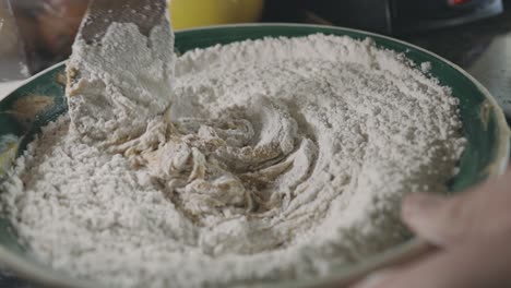 mixing flour and cookie dough mixture with a wooden spoon in the kitchen - close up