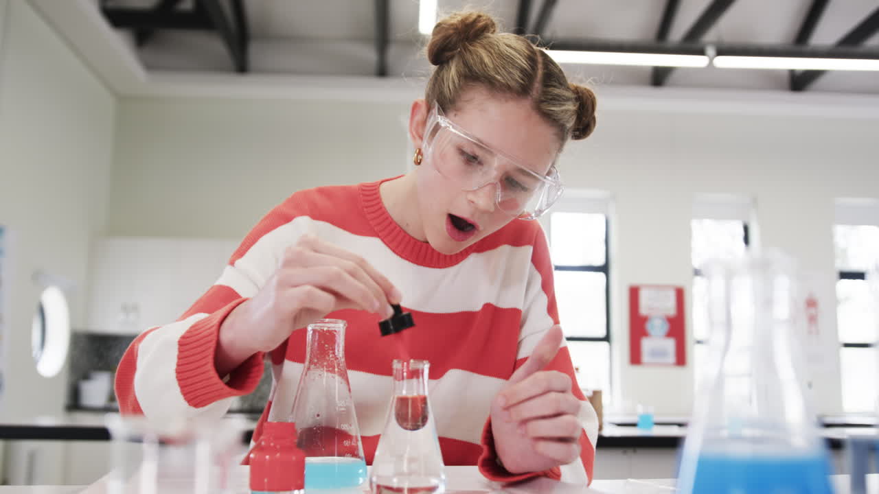 Conducting science experiment in school, young girl wearing safety goggles and focused
