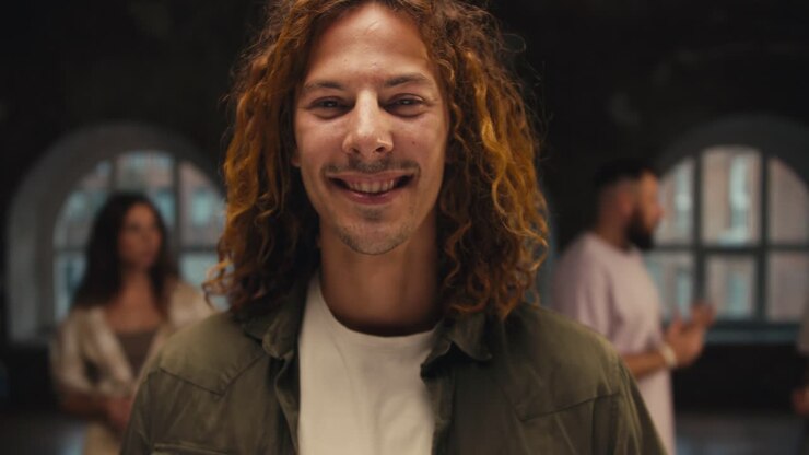 Portrait of a Happy male psychologist with curly hair in a Green jacket who poses against the background of his group during group therapy with a psychologist