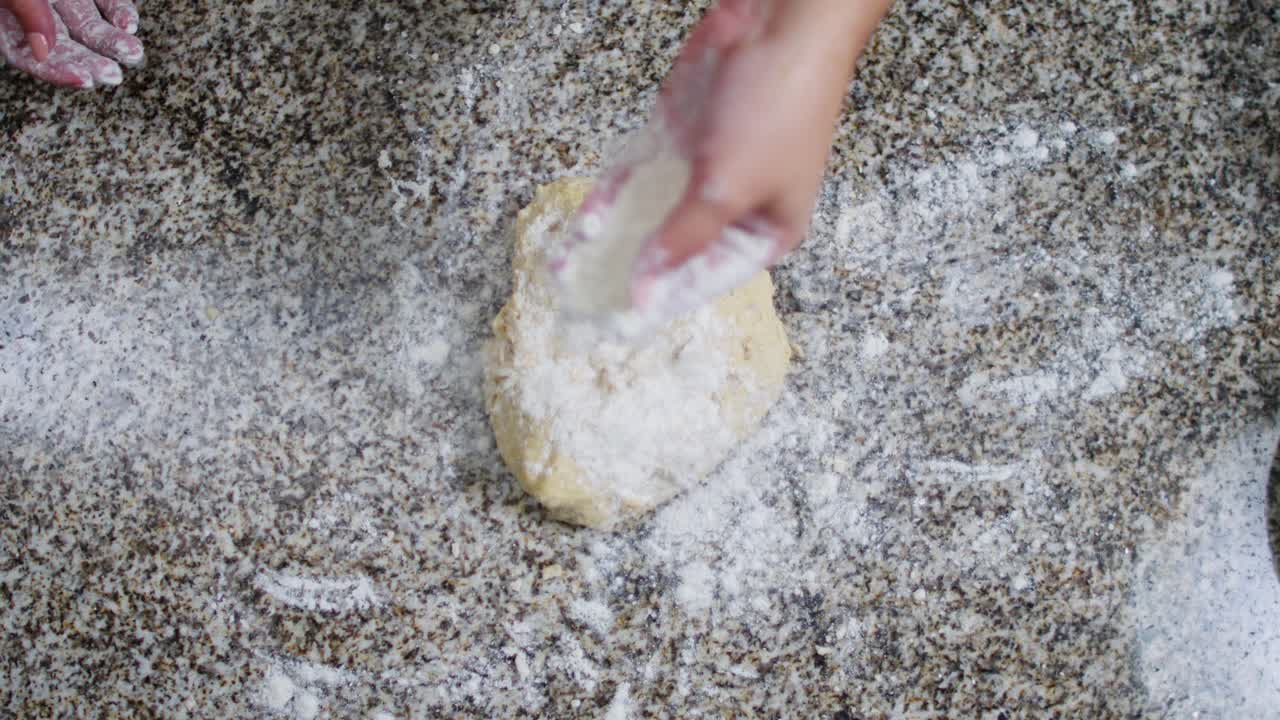 Top view of a woman dusting flour on a dough ball in a kitchen.
