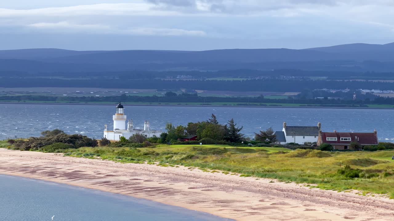 Slow lateral pan of lighthouse, cottages, and beach under soft daylight, Highland landscape in background