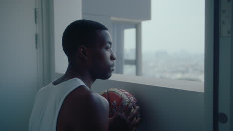 black man with basketball looking at cityscape through hallway window