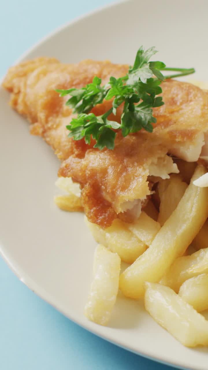 Video close up of fish and chips, parsley and bowl of ketchup on plate, with copy space on blue