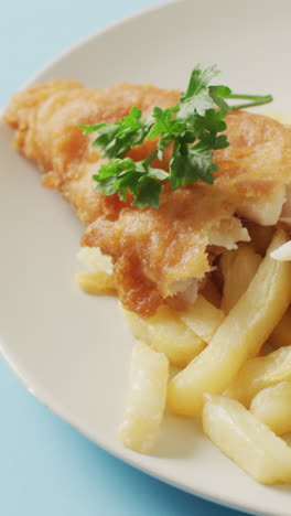 video close up of fish and chips, parsley and bowl of ketchup on plate, with copy space on blue