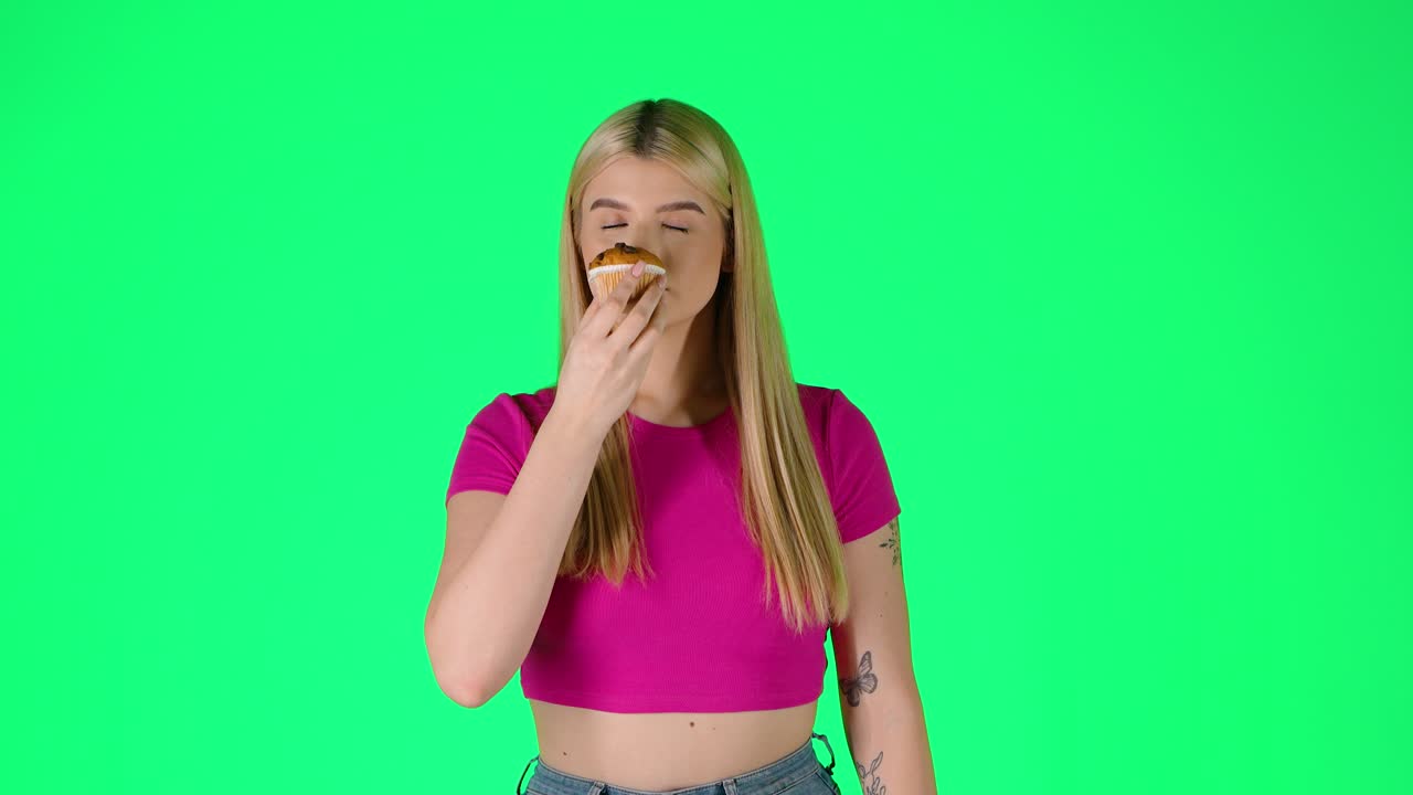 joven mujer rubia oliendo pastel de muffins, olor y sabor ilustración, retrato de estudio con fondo verde